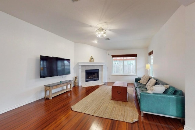 living room featuring visible vents, baseboards, wood finished floors, and a tile fireplace