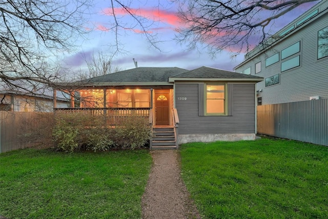 view of front of house featuring entry steps, fence, and a lawn