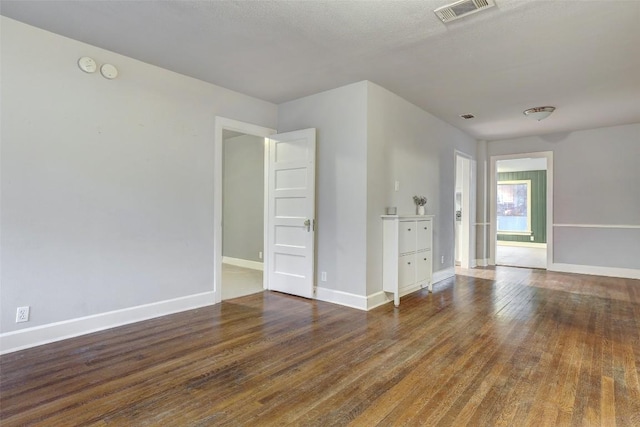 spare room featuring baseboards, visible vents, and dark wood finished floors