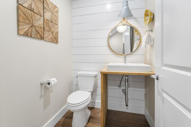 half bathroom with baseboards, vanity, toilet, and wood finished floors