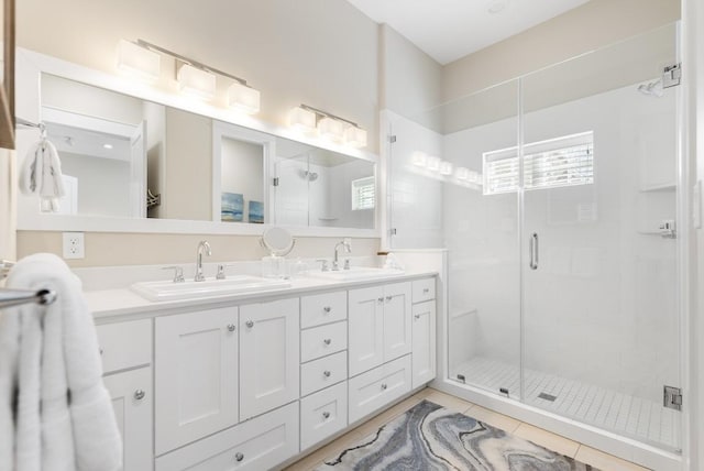 full bath featuring a stall shower, double vanity, a sink, and tile patterned floors