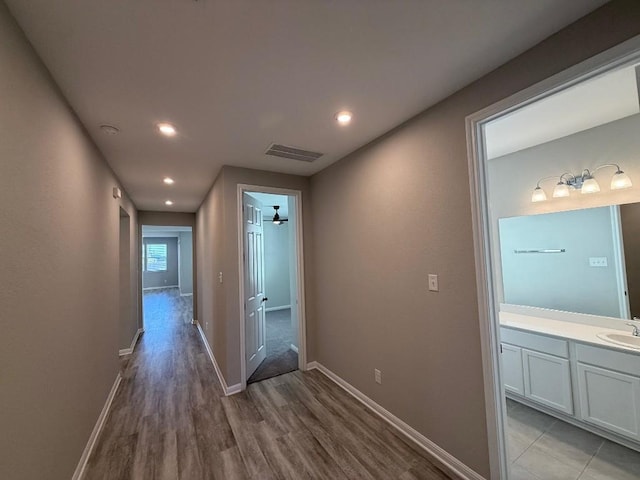 corridor with baseboards, visible vents, light wood-style flooring, and a sink