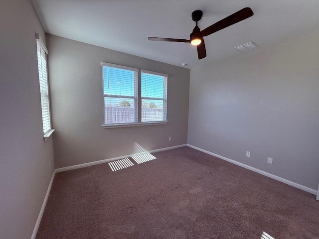 unfurnished room with ceiling fan, dark colored carpet, visible vents, and baseboards