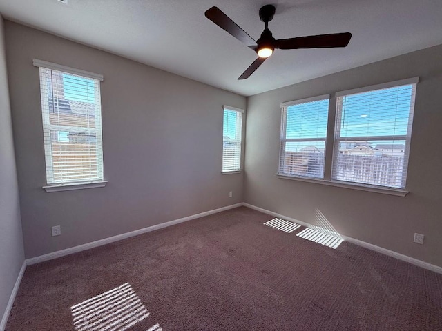 unfurnished room featuring baseboards, dark colored carpet, and a ceiling fan