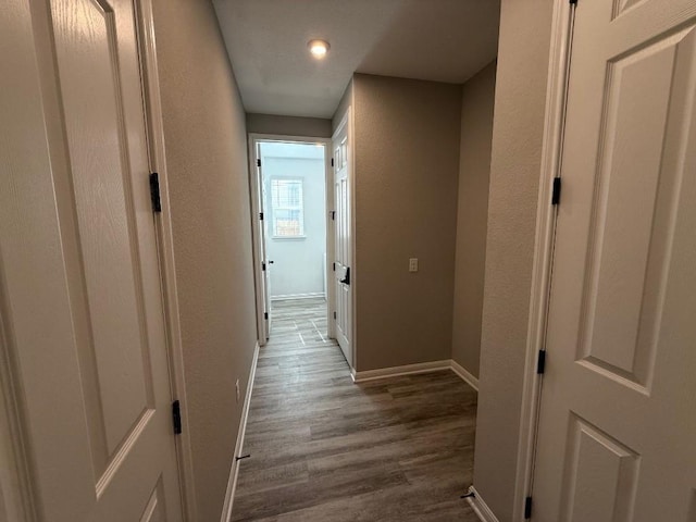 hallway with a textured wall, wood finished floors, and baseboards