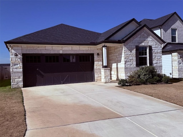 view of front of house with concrete driveway, stone siding, an attached garage, and a shingled roof