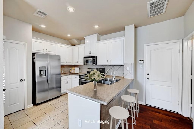 kitchen featuring stainless steel appliances, a peninsula, a sink, visible vents, and white cabinets