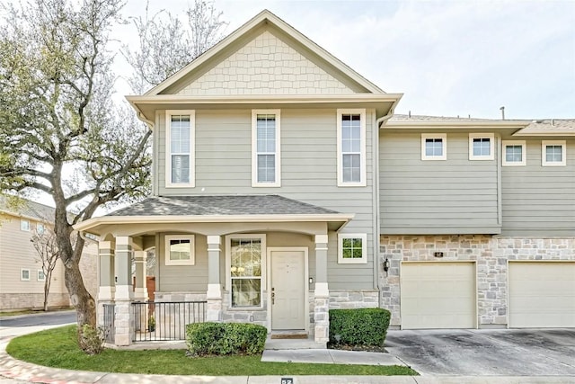 townhome / multi-family property with roof with shingles, covered porch, a garage, stone siding, and driveway