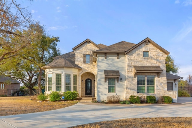 french provincial home with driveway, fence, and roof with shingles