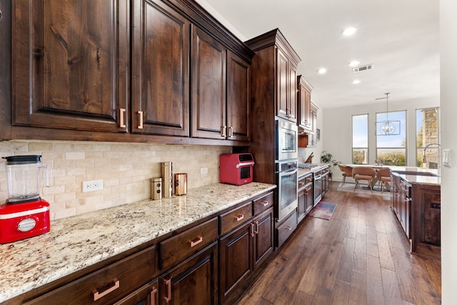 kitchen featuring light stone counters, stainless steel appliances, visible vents, tasteful backsplash, and dark wood finished floors