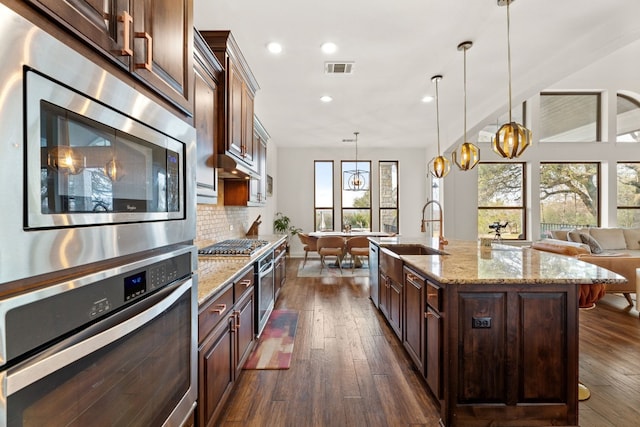 kitchen with light stone counters, a sink, appliances with stainless steel finishes, tasteful backsplash, and dark wood finished floors