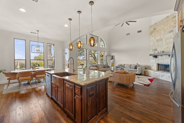 kitchen with light stone counters, appliances with stainless steel finishes, dark wood-type flooring, a fireplace, and a sink