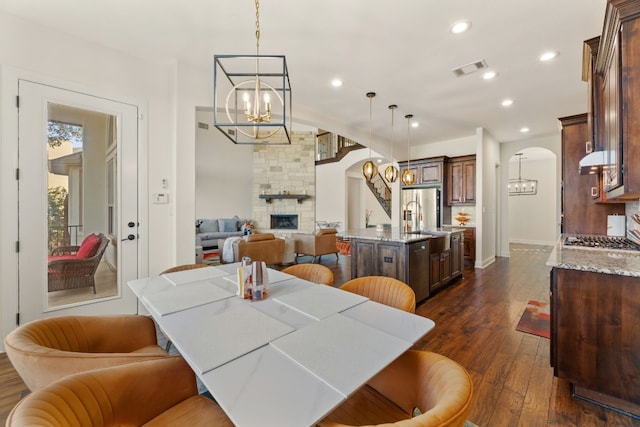 dining space with arched walkways, dark wood-type flooring, a fireplace, a chandelier, and recessed lighting