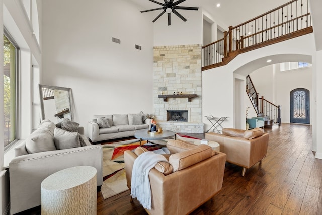 living room featuring arched walkways, dark wood-type flooring, a fireplace, visible vents, and stairway