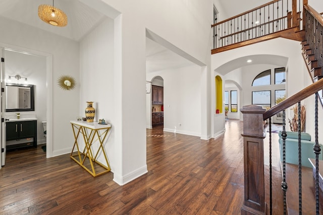 entryway with baseboards, arched walkways, dark wood-type flooring, a high ceiling, and stairs