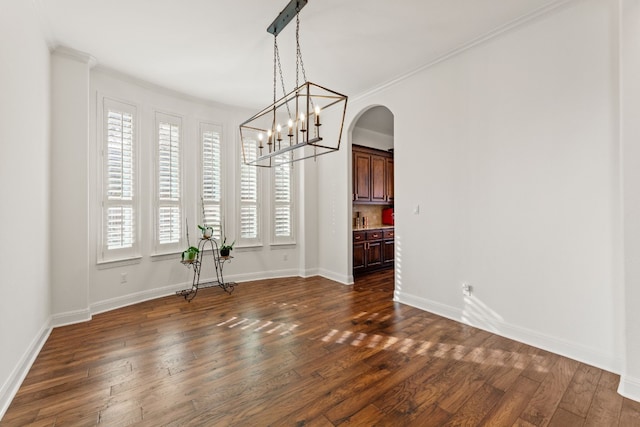 unfurnished dining area with ornamental molding, arched walkways, dark wood-style flooring, and baseboards