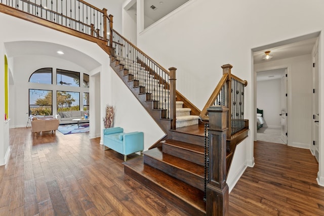 staircase with arched walkways, baseboards, a high ceiling, and wood finished floors