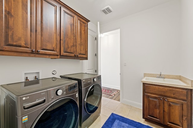 washroom featuring light tile patterned flooring, a sink, visible vents, washer and dryer, and cabinet space