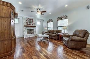 living room featuring dark wood-type flooring, a fireplace, a ceiling fan, and a healthy amount of sunlight