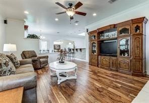 living room with dark wood-type flooring, visible vents, ornamental molding, and a ceiling fan