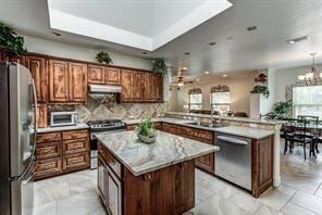 kitchen featuring a kitchen island, a peninsula, stainless steel appliances, light countertops, and under cabinet range hood