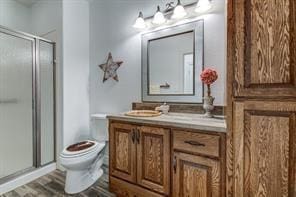 bathroom with toilet, a stall shower, wood finished floors, and vanity