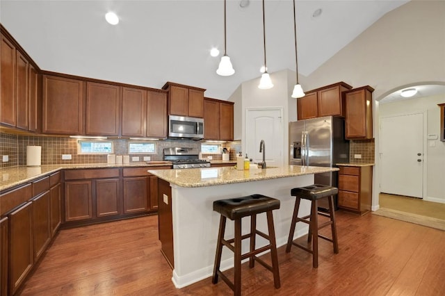 2405 Billy Pat Rd, Leander, TX 78641 - kitchen featuring appliances with stainless steel finishes, arched walkways, wood finished floors, decorative backsplash, and high vaulted ceiling