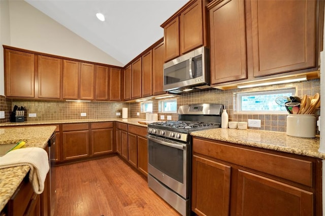 2405 Billy Pat Rd, Leander, TX 78641 - kitchen with appliances with stainless steel finishes, light wood-style floors, vaulted ceiling, backsplash, and light stone counters