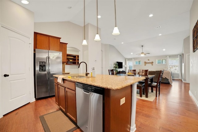 2405 Billy Pat Rd, Leander, TX 78641 - kitchen with stainless steel appliances, ceiling fan, brown cabinetry, light wood finished floors, and a center island with sink