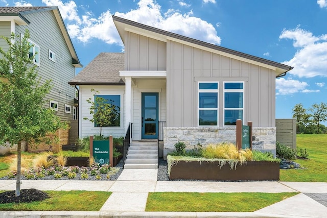 view of front of property featuring board and batten siding, stone siding, and a shingled roof