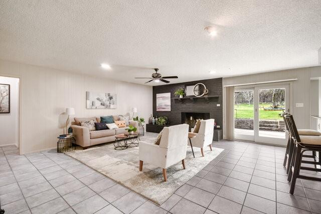 living room with ceiling fan, a textured ceiling, a fireplace, and light tile patterned flooring