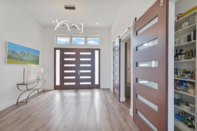 foyer featuring light wood-type flooring, a barn door, baseboards, and a notable chandelier