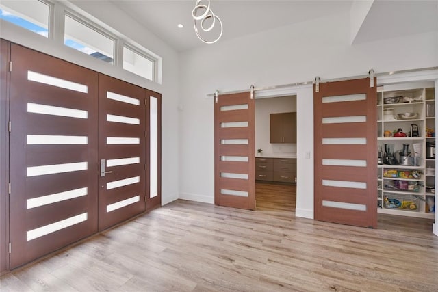 entrance foyer with light wood-type flooring, a barn door, baseboards, and french doors