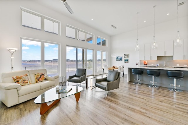 living area with a towering ceiling, a water view, light wood-style flooring, and visible vents