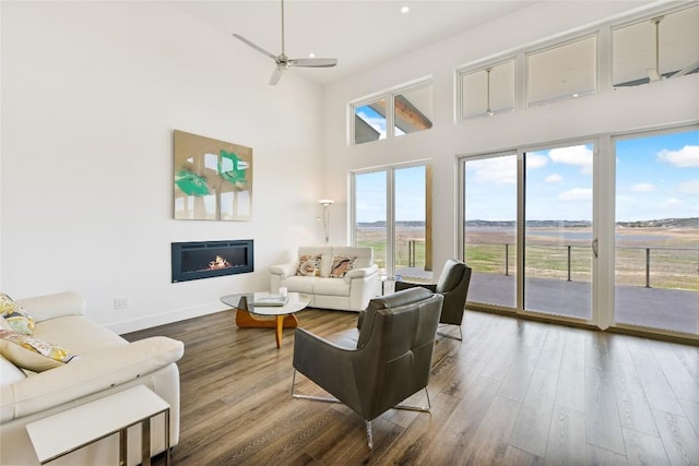 living room with a glass covered fireplace, baseboards, a high ceiling, and wood finished floors