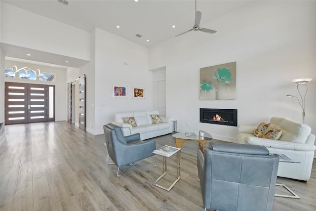 living area with light wood finished floors, a high ceiling, a ceiling fan, a warm lit fireplace, and baseboards