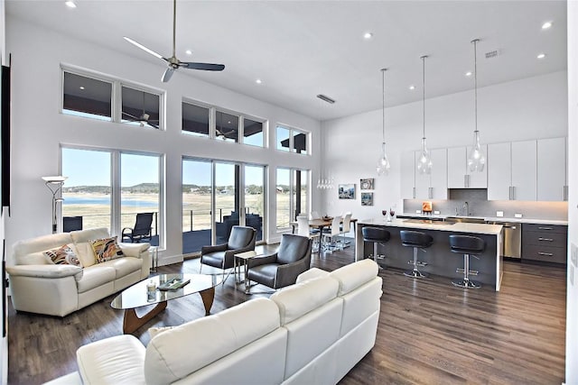 living area featuring recessed lighting, a water view, visible vents, a high ceiling, and dark wood-type flooring