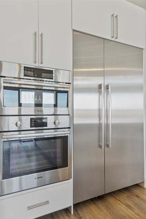 kitchen with stainless steel appliances, wood finished floors, and white cabinetry