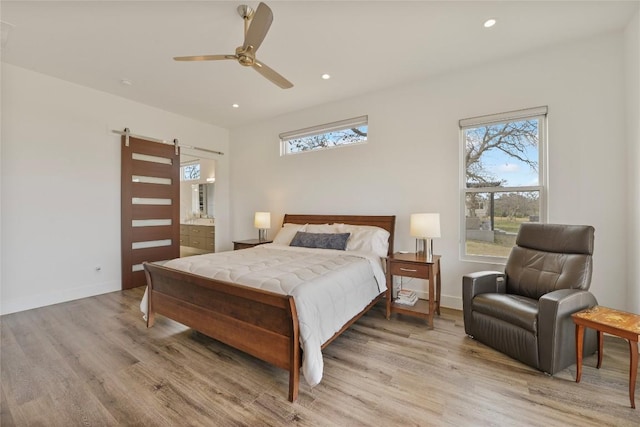 bedroom with a barn door, baseboards, connected bathroom, light wood-style floors, and recessed lighting