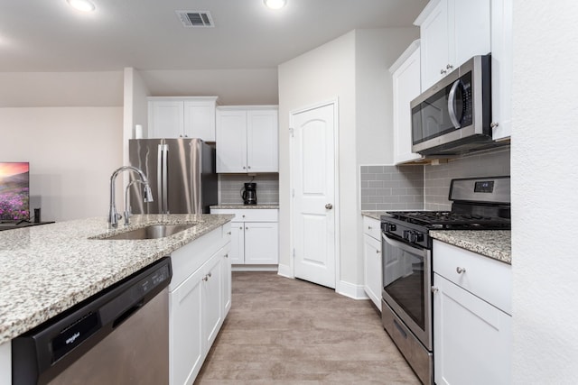 kitchen with visible vents, appliances with stainless steel finishes, white cabinetry, a sink, and light stone countertops