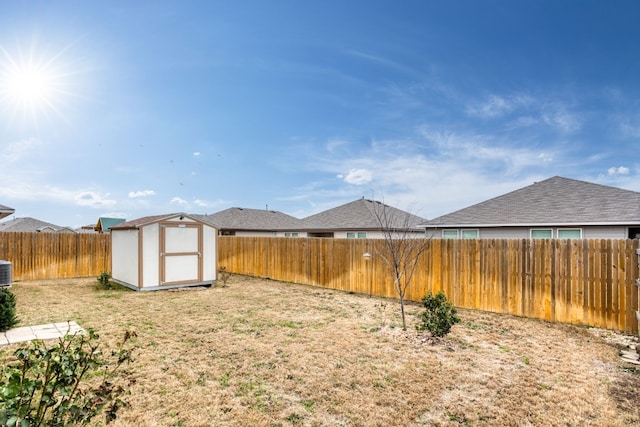 view of yard with an outbuilding, a fenced backyard, central AC unit, and a storage unit