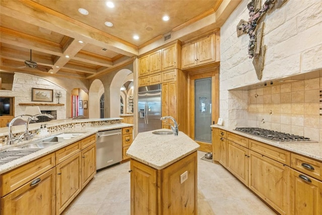 kitchen with coffered ceiling, an island with sink, a sink, stainless steel appliances, and backsplash