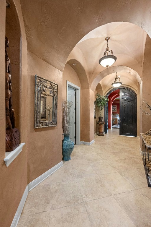 corridor featuring lofted ceiling, arched walkways, and baseboards