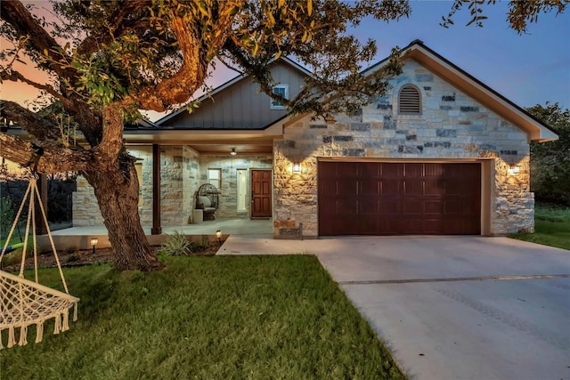 view of front facade featuring concrete driveway, stone siding, an attached garage, board and batten siding, and a front yard