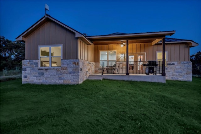 back of house with stone siding, a lawn, board and batten siding, and a standing seam roof