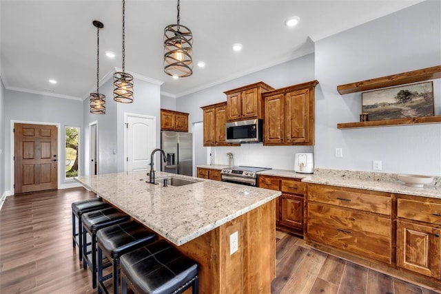 kitchen featuring stainless steel appliances, pendant lighting, brown cabinetry, and a center island with sink