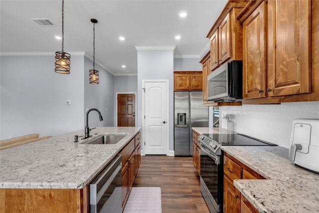 kitchen featuring light stone counters, decorative light fixtures, a sink, appliances with stainless steel finishes, and a center island with sink