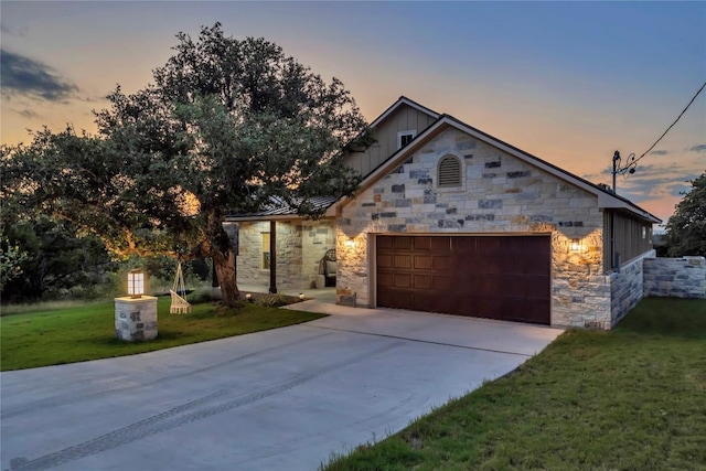 view of front of house featuring a garage, stone siding, a lawn, and concrete driveway