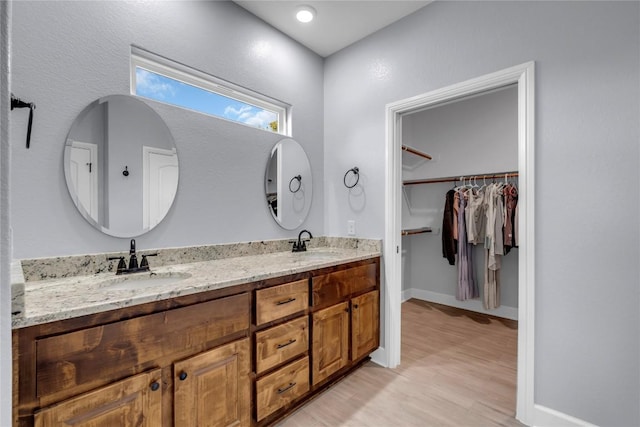 bathroom with a sink, double vanity, wood finished floors, and a walk in closet