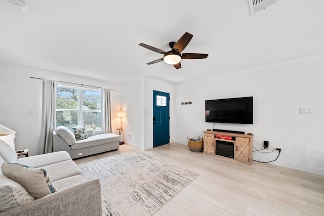 living room featuring baseboards, visible vents, ceiling fan, and light wood finished floors